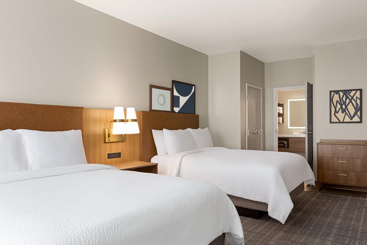 Een hotelkamer met twee bedden, een nachtkastje met lamp, een dressoir en een deur naar de badkamer.