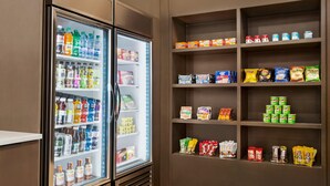 Een gekoelde drankautomaat gevuld met diverse dranken en een schap met snacks en verpakte producten.