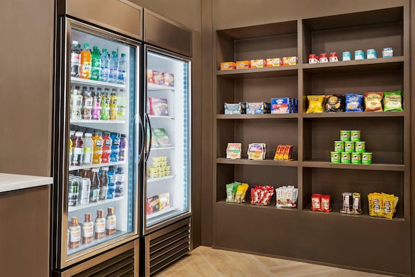 Een gekoelde drankautomaat gevuld met diverse dranken en een schap met snacks en verpakte producten.