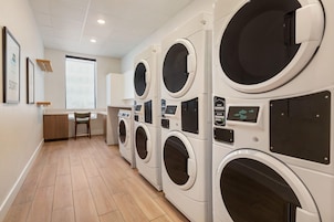 A laundry facility with multiple washing machines, a wooden floor, and a window providing natural light.