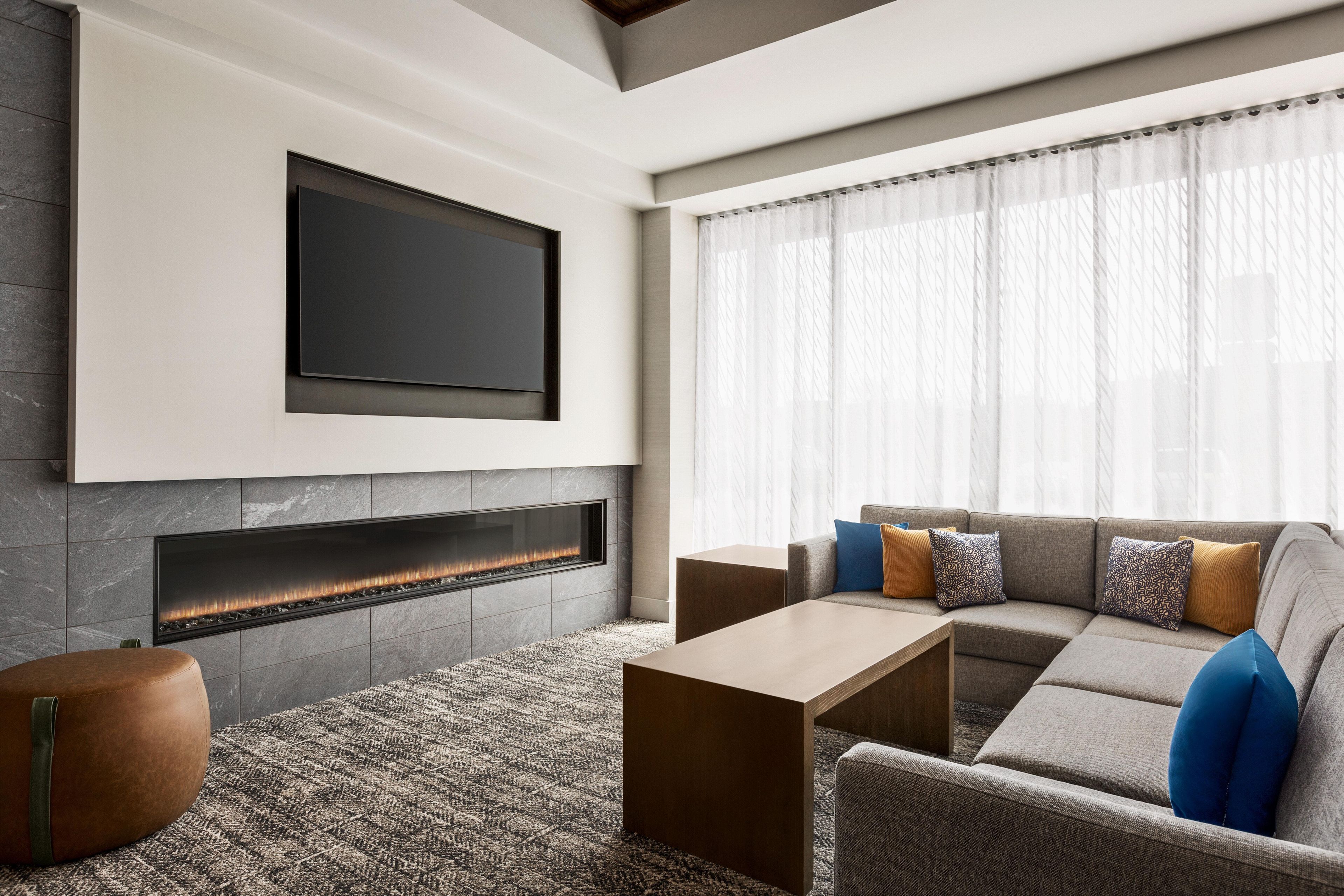 A modern living room with a flat-screen TV mounted above a fireplace, a sectional sofa with cushions, and a coffee table.