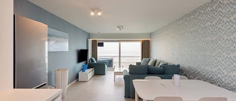 Una sala de estar moderna con un televisor de pantalla plana, una mesa de comedor con sillas, un sofá y un amplio ventanal con vistas.