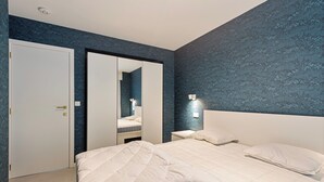 Une chambre avec deux lits, une armoire, un miroir et une table de chevet avec une lampe.