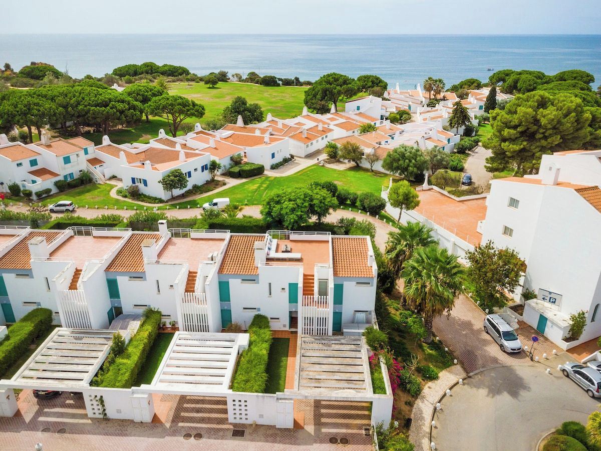 Zona residencial costera con edificios blancos, césped verde y vista al mar.
