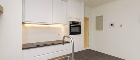 Una cocina moderna con armarios blancos, un lavamanos de acero inoxidable y un horno empotrado.