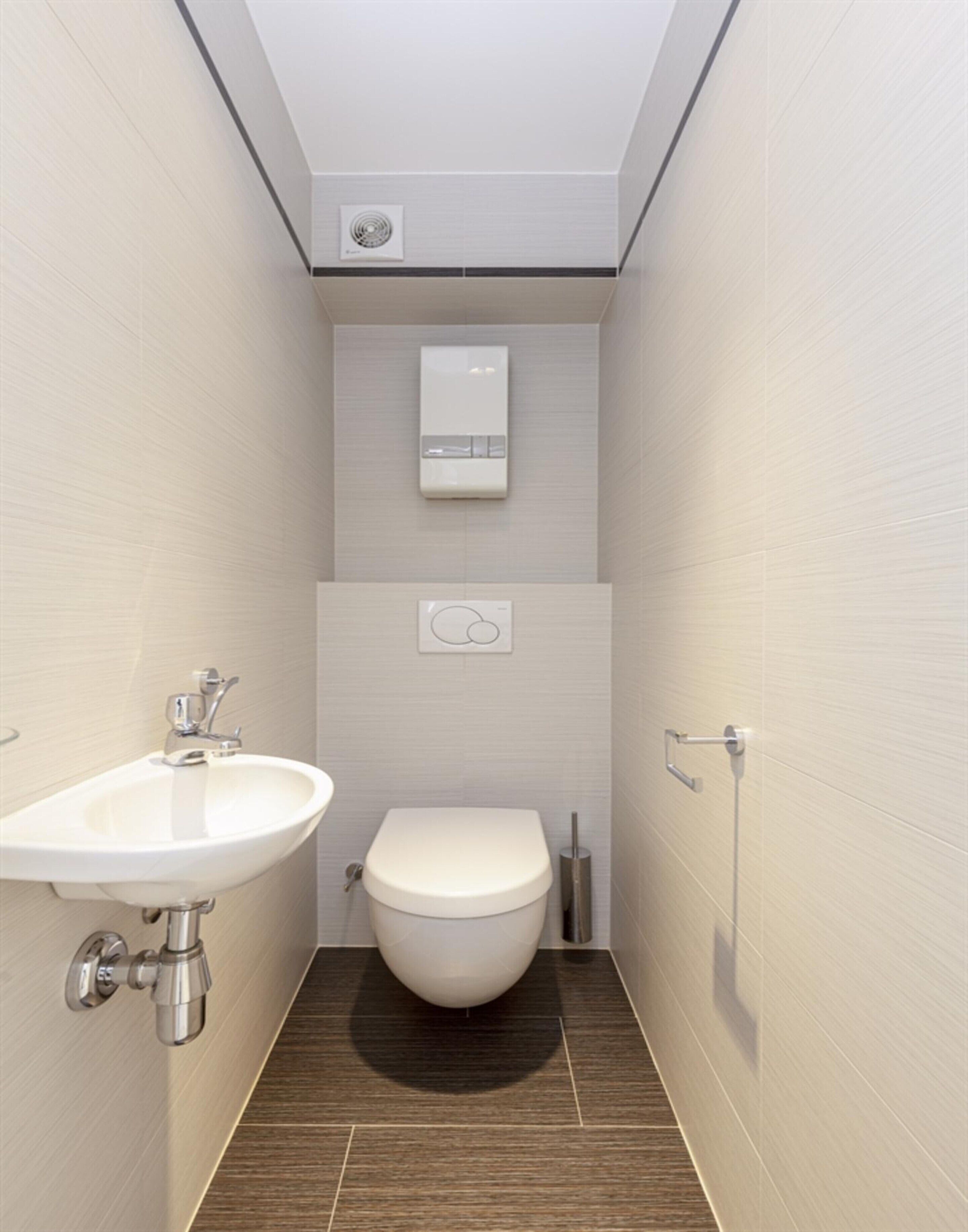 A modern bathroom with a white sink, toilet, and a wall-mounted heater.