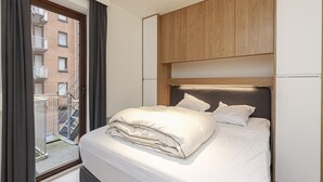 A modern bedroom with a large bed, wooden headboard, and a view of a balcony. - Apartment in Blankenberge Near Marina (Blankenberge)