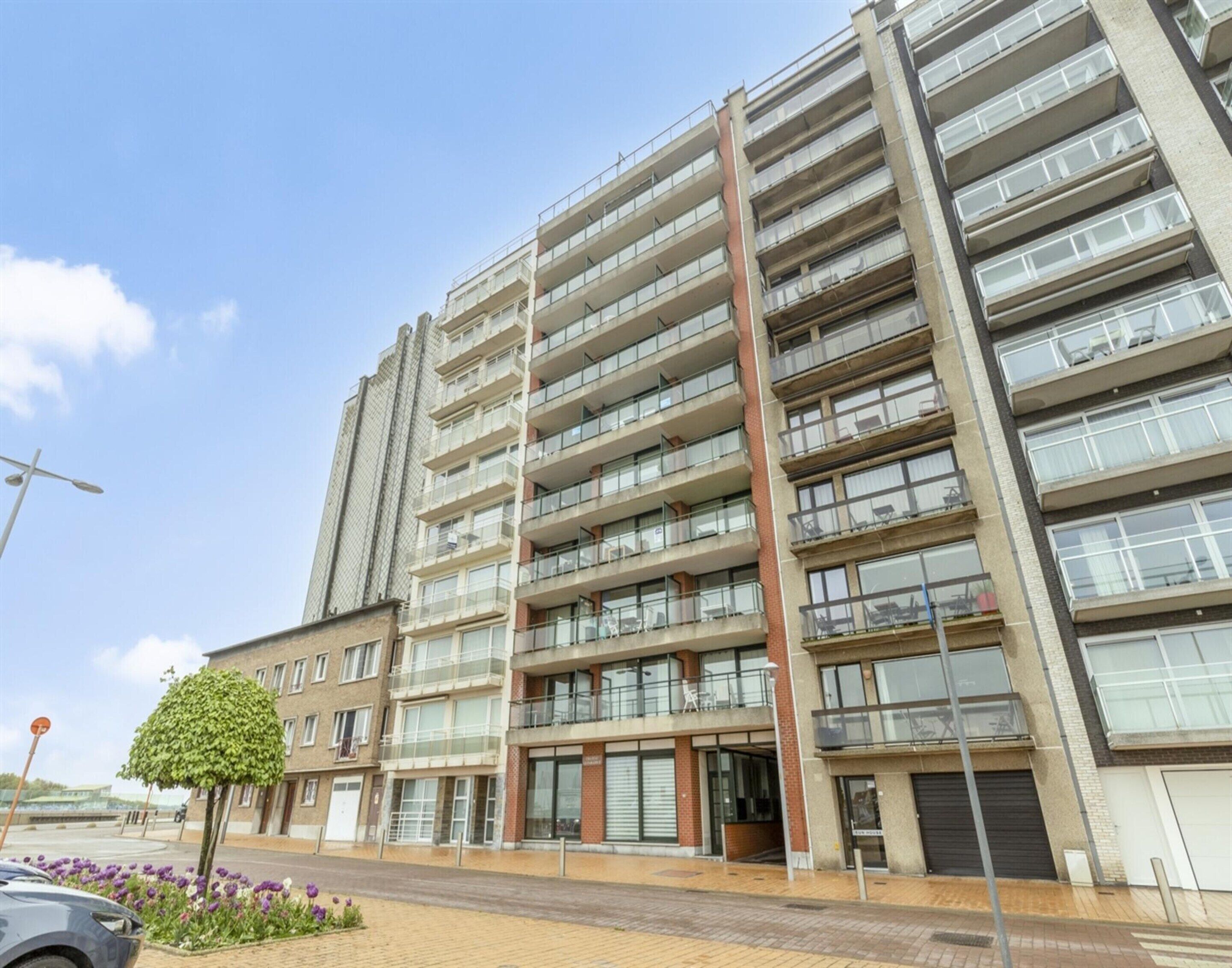 A multi-story residential building with balconies, large windows, and a brick facade.