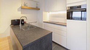 A modern kitchen with a grey countertop, white cabinets, and a built-in oven. - Apartment in Blankenberge Near Marina (Blankenberge)