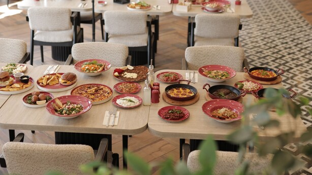 A restaurant with multiple tables and chairs, each set with plates of food and cutlery. - Elite World GO  İnegöl  (Inegol)
