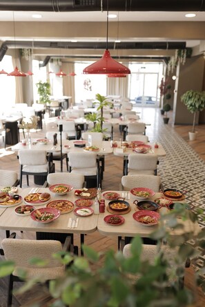 A restaurant with multiple tables and chairs, each set with plates of food and cutlery. - Elite World GO  İnegöl  (Inegol)