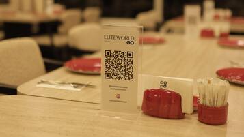 L’intérieur d’un restaurant, avec des tables dressées pour le service, un menu accessible via un code QR et des récipients rouges contenant des condiments.