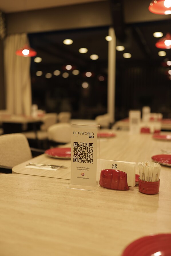 A restaurant interior with tables set for dining, QR code menu, and red condiment containers. - Elite World GO  İnegöl  (Inegol)