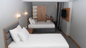 A hotel room with two single beds, a wardrobe, a small table with a lamp, and a flat-screen TV mounted on the wall. - Elite World GO  İnegöl  (Inegol)