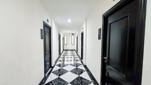 Un couloir au sol carrelé de noir et de blanc, aux murs blancs, et avec des portes de part et d’autre.