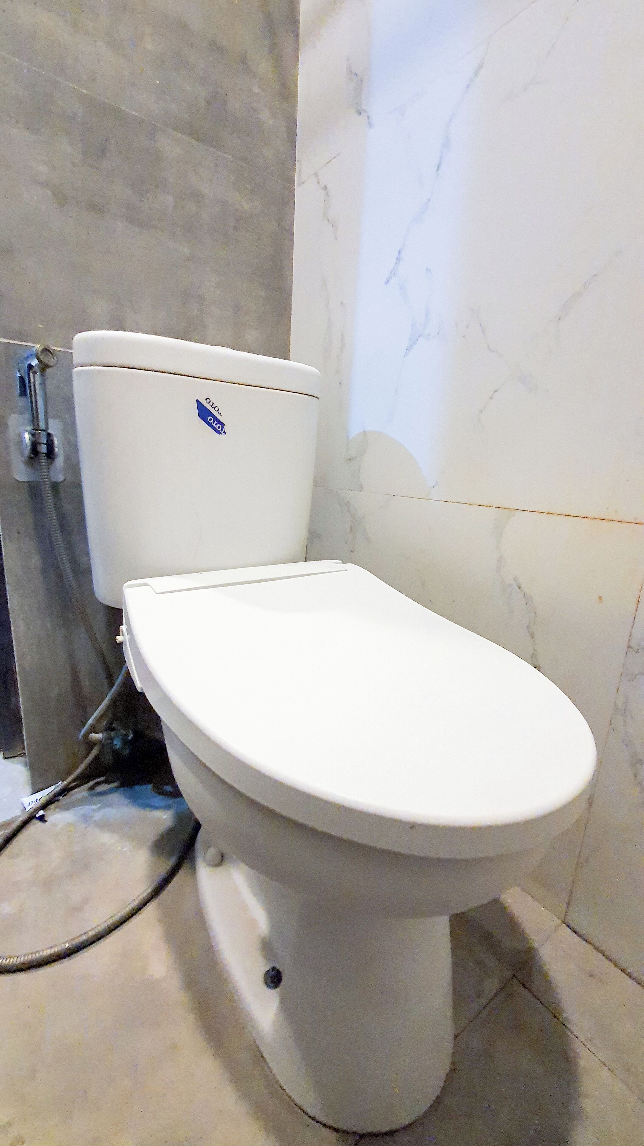 A white toilet with a blue sticker, a visible pipe, and a tiled wall with a crack.