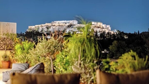 A view of a building on a hill with a patio area in the foreground.