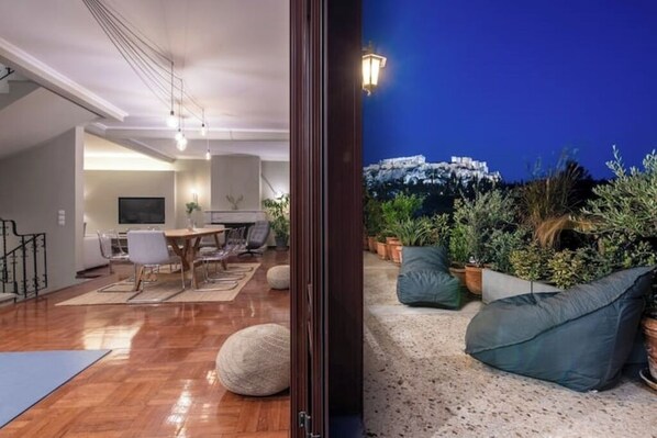 A modern living room with a dining area, a staircase, and a view of a historic building at night.