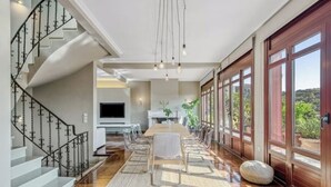 A spacious dining area with a long table, clear chairs, and a staircase on the left.