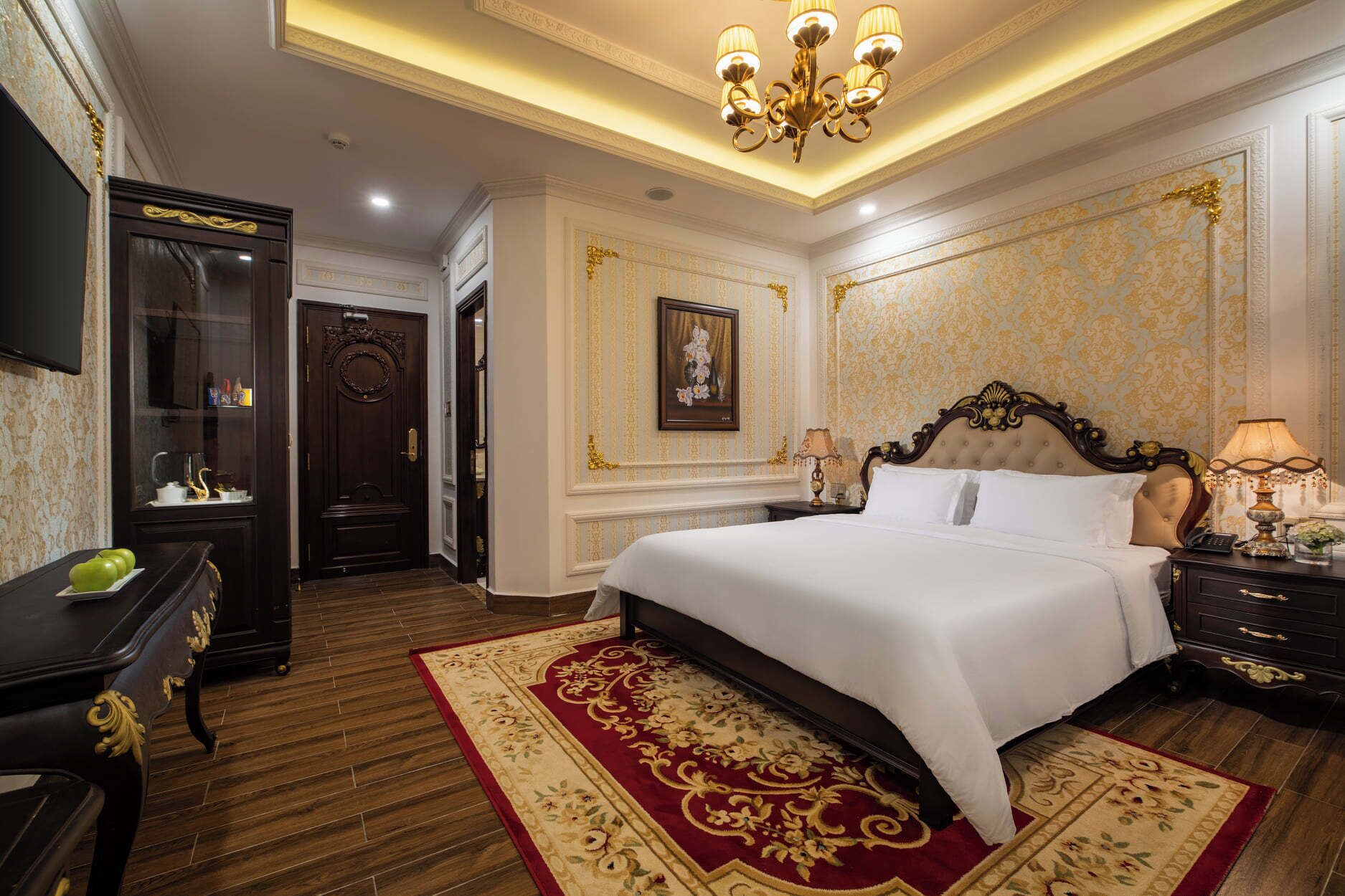 A luxurious hotel room with a large bed, a wooden floor, a chandelier, and ornate wall decorations.