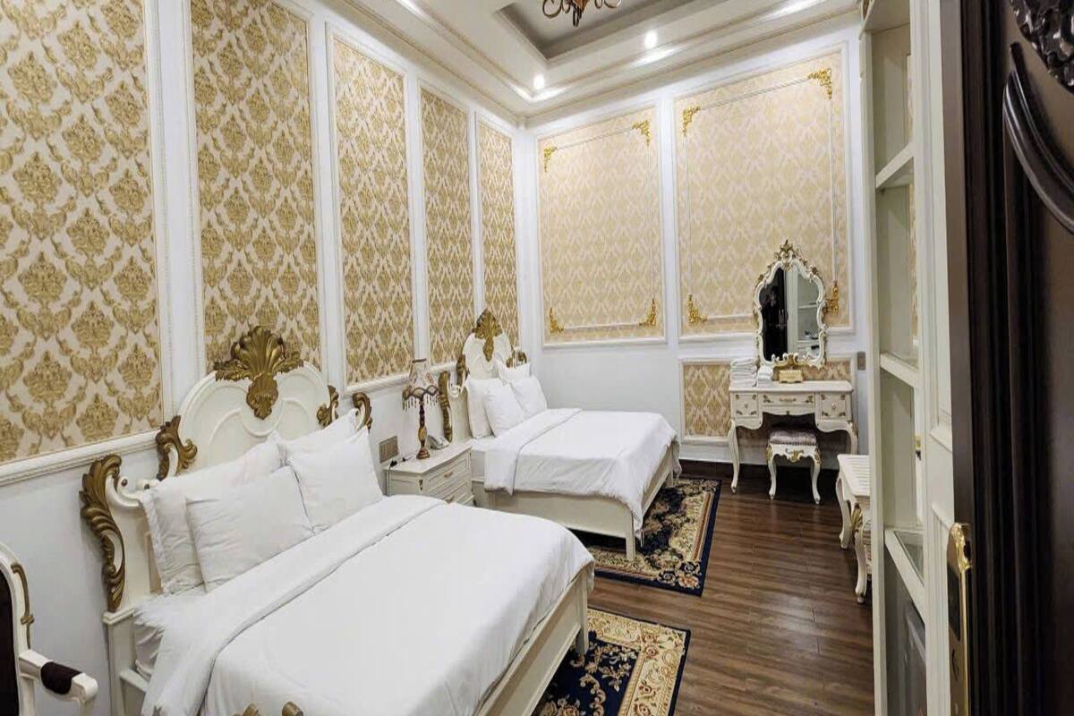 Un dormitorio lujoso con dos camas grandes, cabeceros ornamentados y un espejo sobre el tocador.