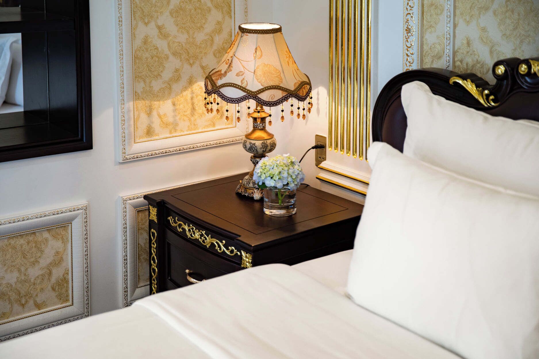 A hotel room with a bed, a nightstand with a lamp, and a framed picture on the wall.