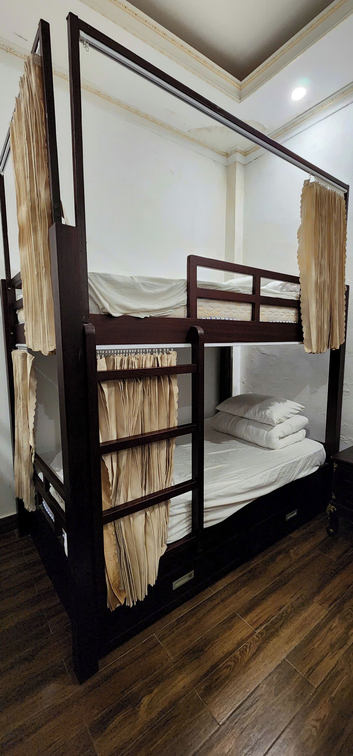 Una cama litera con cortinas, piso de madera y pared blanca.