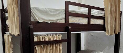 Una cama litera con cortinas, piso de madera y pared blanca.