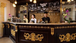 A coffee shop counter with three baristas, a menu board, and decorative lighting. - Dream Boutique Hotel Da Lat (Xuan Huong - Da Lat)