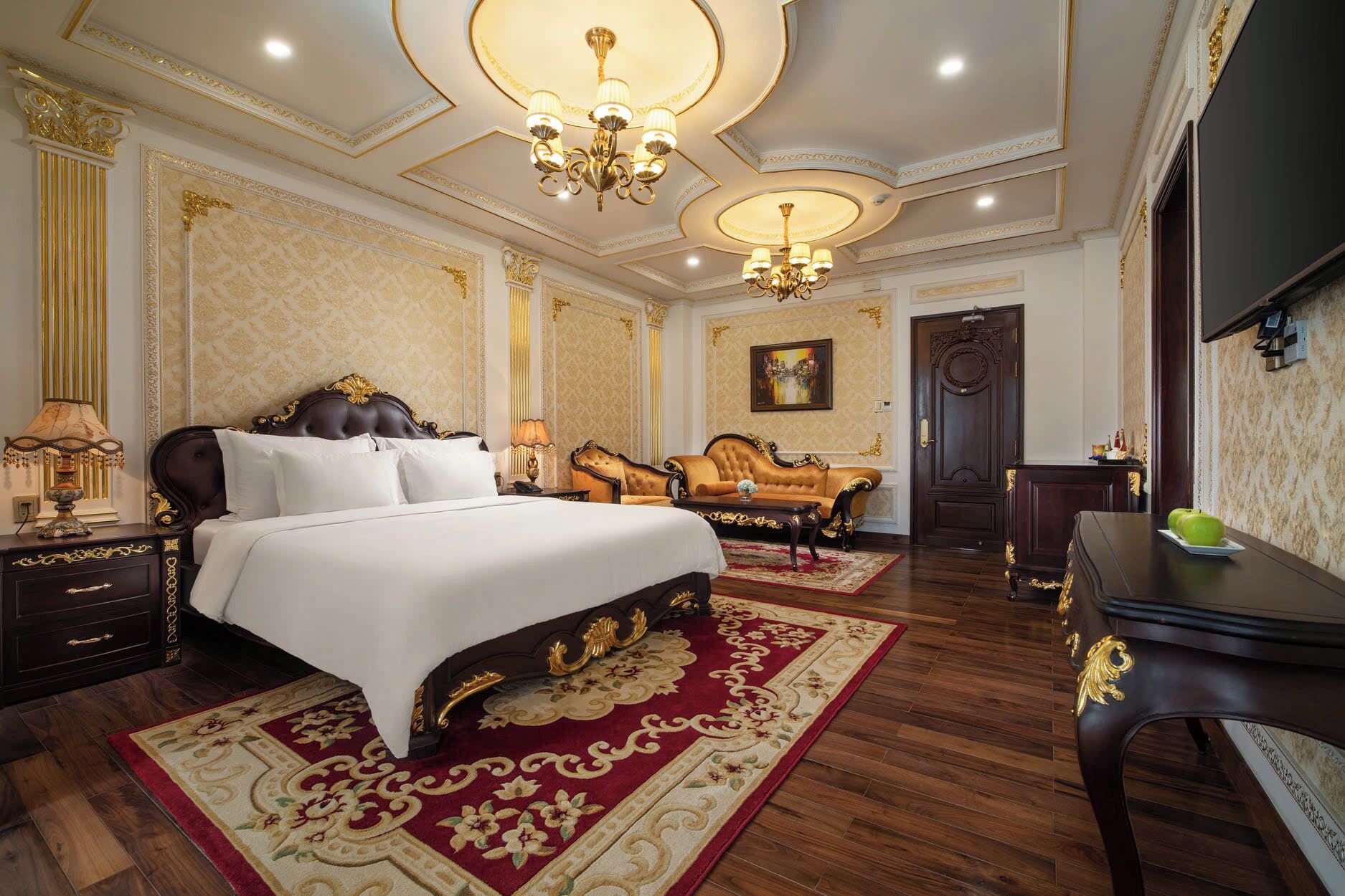 A luxurious bedroom with a large bed, two armchairs, a desk, and a chandelier.