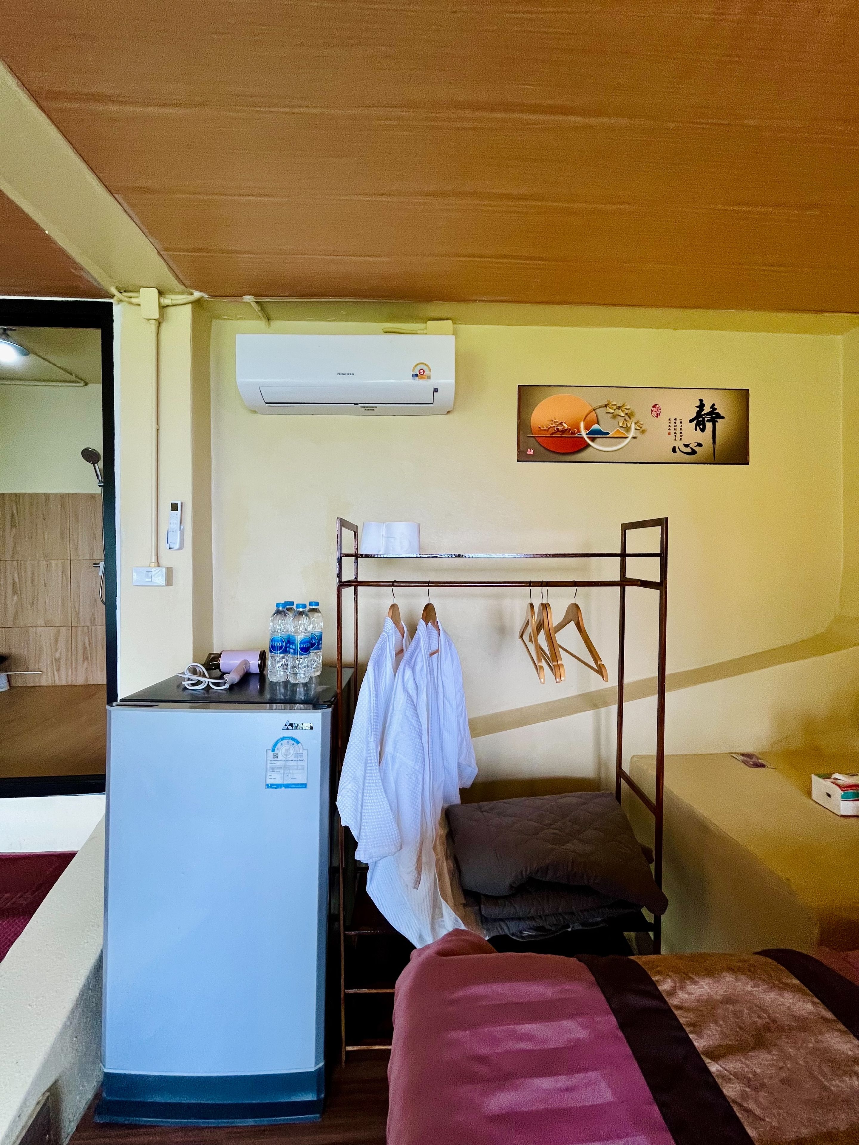 A room with a bunk bed, a small desk with a refrigerator, and a wall-mounted air conditioner.