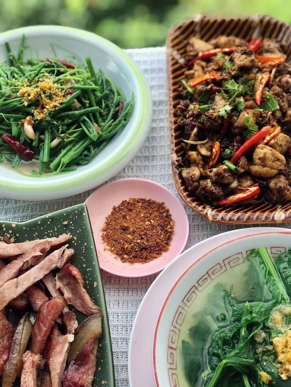 A variety of dishes including stir-fried meat, green vegetables, and a bowl of soup.