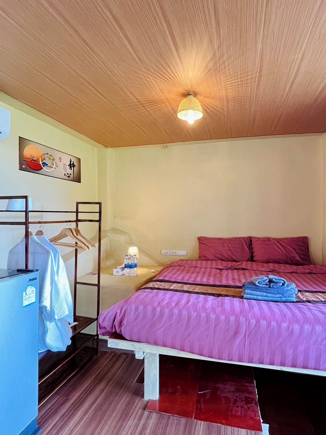 Habitació d'hotel amb llit, armari, escriptori amb làmpada i prestatge fixat a la paret.