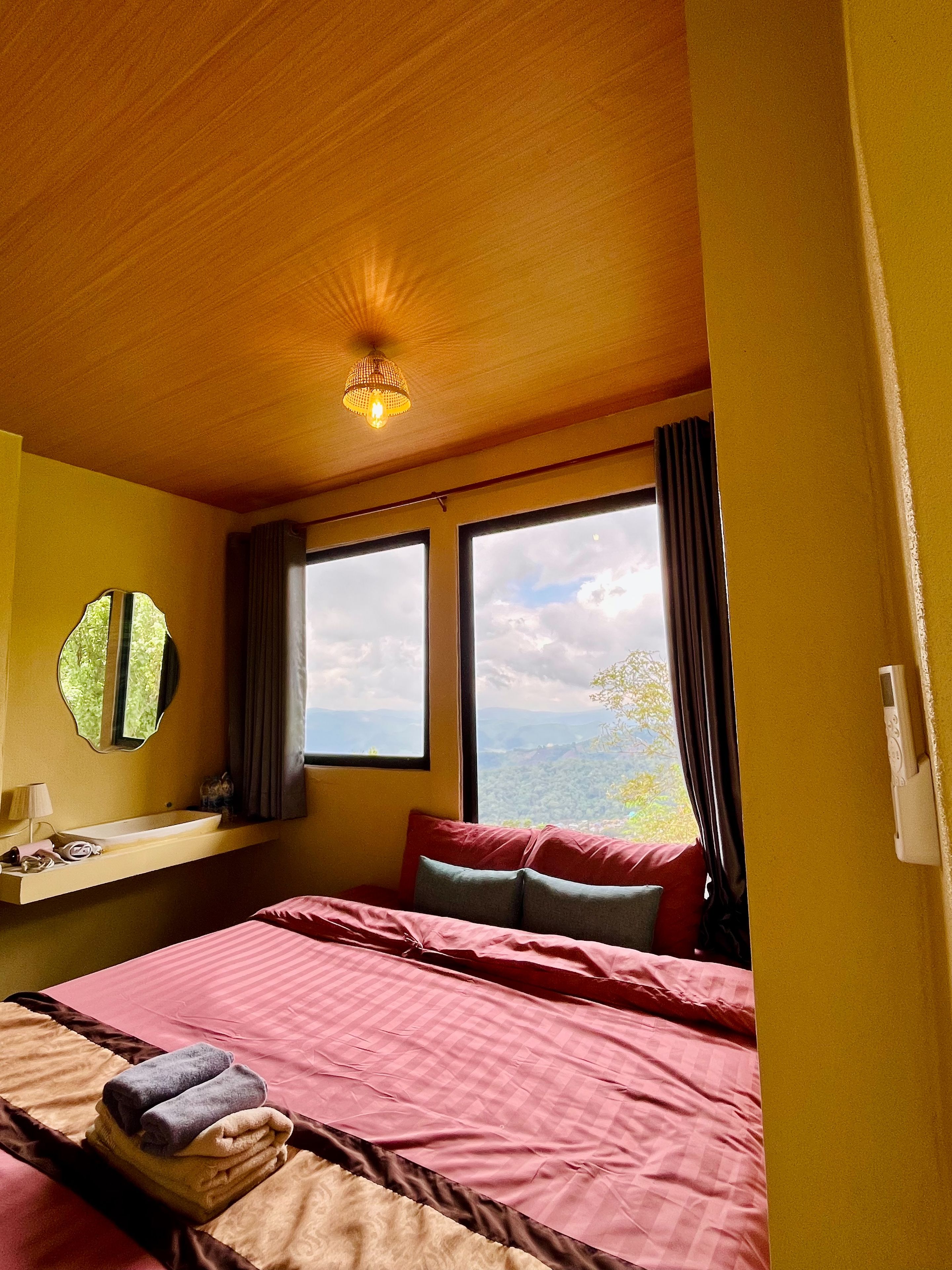 Ein Hotelzimmer mit Bett, Nachttisch, Spiegel und Fenster mit Blick ins Freie.