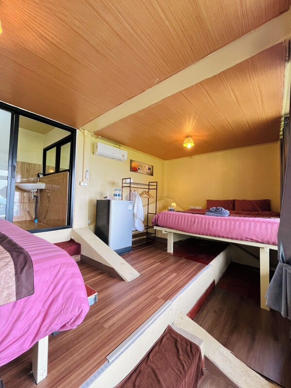 A compact room with two beds, a small kitchenette, and a bathroom with a mirror.