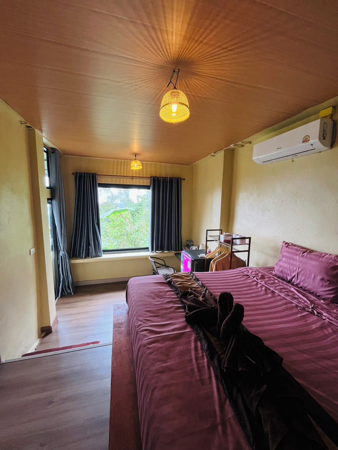 A hotel room with a bed, a desk, a chair, an air conditioning unit, and a window with curtains.