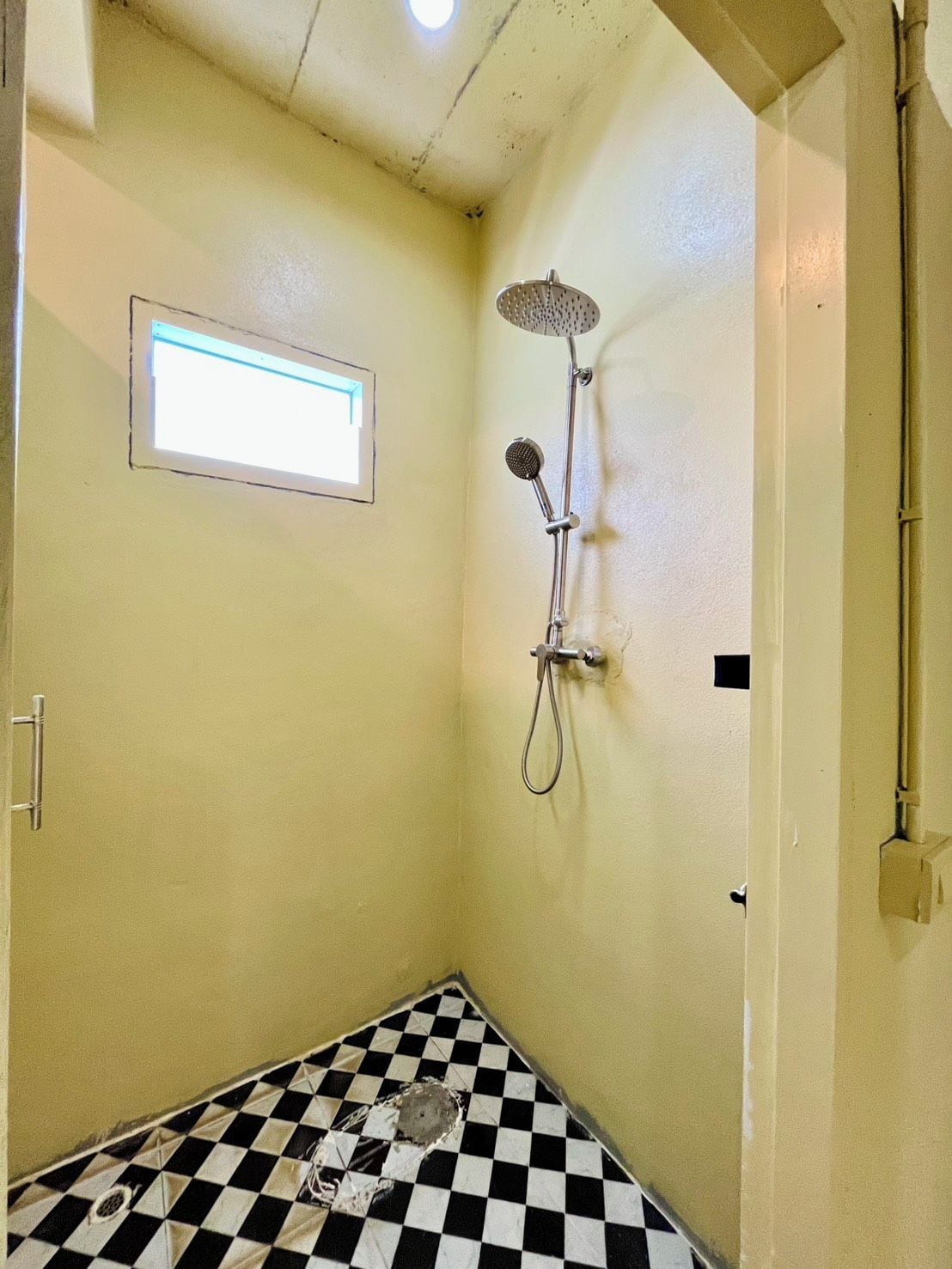 A small bathroom with a shower, a checkered floor, and a window.
