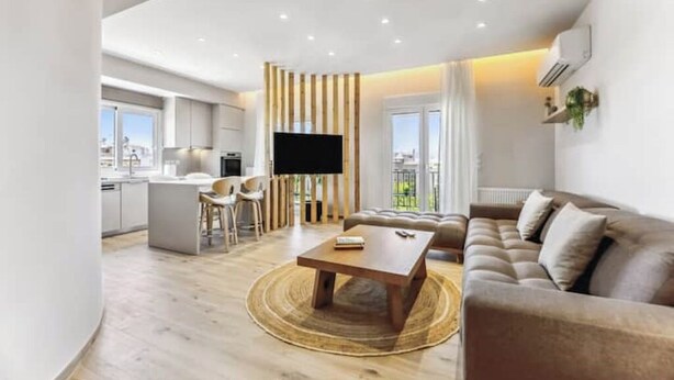 Een moderne woonkamer met een bank, salontafel en televisie. Er is een keukenhoek met een eettafel en stoelen. De kamer heeft grote ramen en uitzicht op de stad.