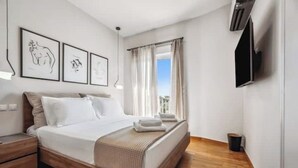 Een moderne hotelkamer met een houten vloer, een groot bed met witte lakens, een flatscreen televisie aan de muur en een raam met gordijnen.