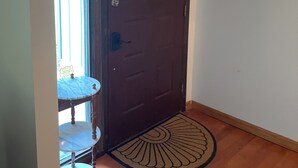 Eine Holztür mit einer Kettenriegel-Verriegelung, ein kleiner Tisch mit einem Stuhl und eine Fußmatte mit Sonnendesign.