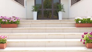 A building with a set of steps leading to a door with a glass panel. There are potted plants on either side of the steps. - Kalispera Residence  (Scalea)