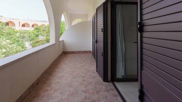 Un pasillo con piso de baldosas, una puerta con marco oscuro y vista a un edificio con arcos al fondo.