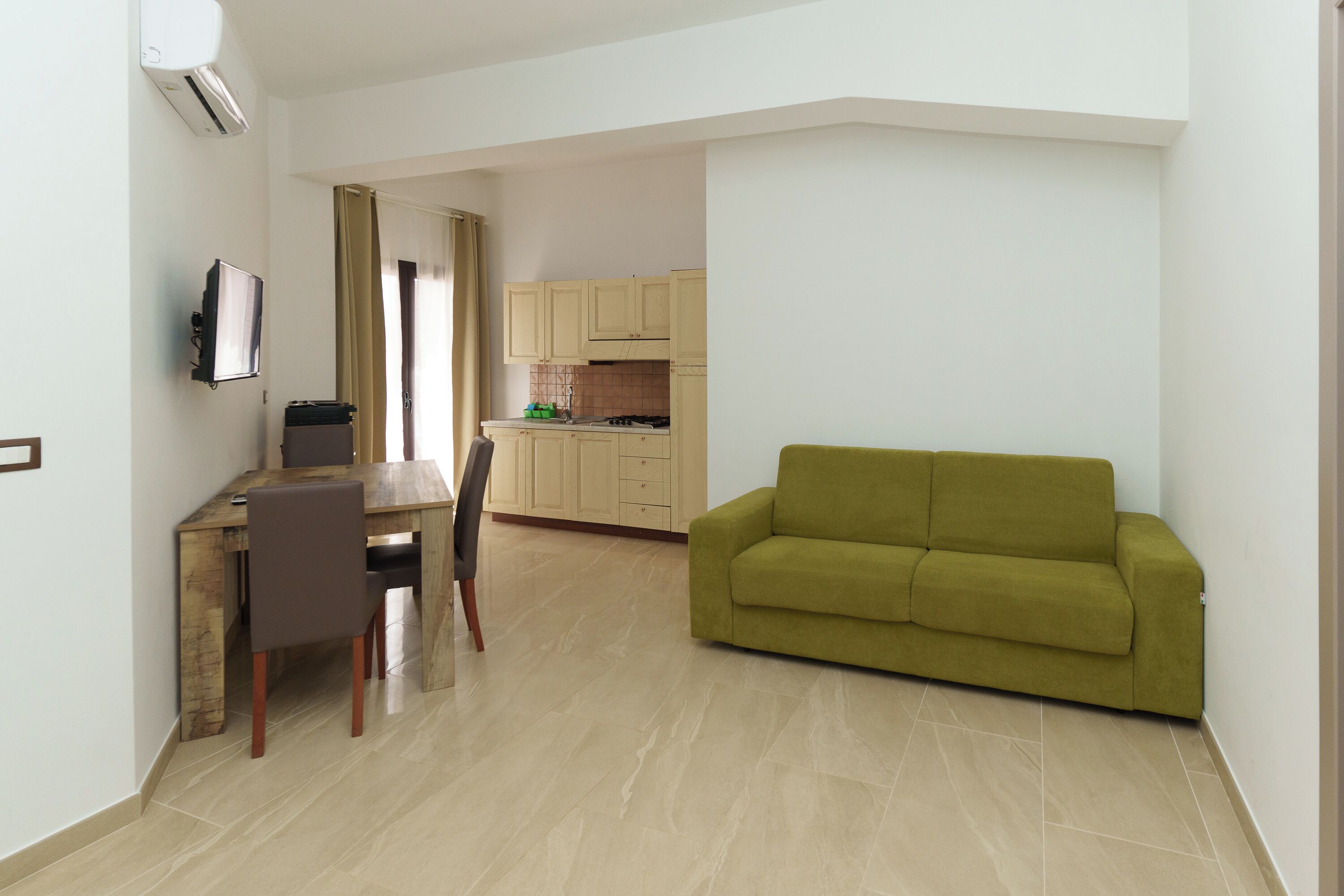 Una sala moderna con un sofá verde, una mesa de comedor de madera con sillas, y una cocina con armarios y estufa.
