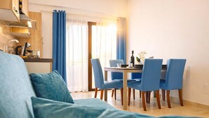 A modern living room with a sofa, a dining table with chairs, and a kitchen area with a stove and cabinets. - Kalispera Residence  (Scalea)