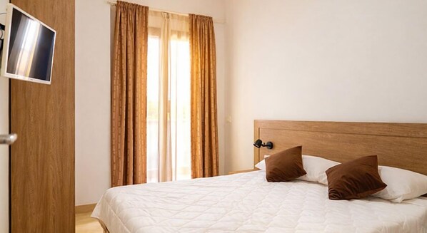 A hotel room with a bed, two pillows, a wooden headboard, and a TV mounted on the wall.