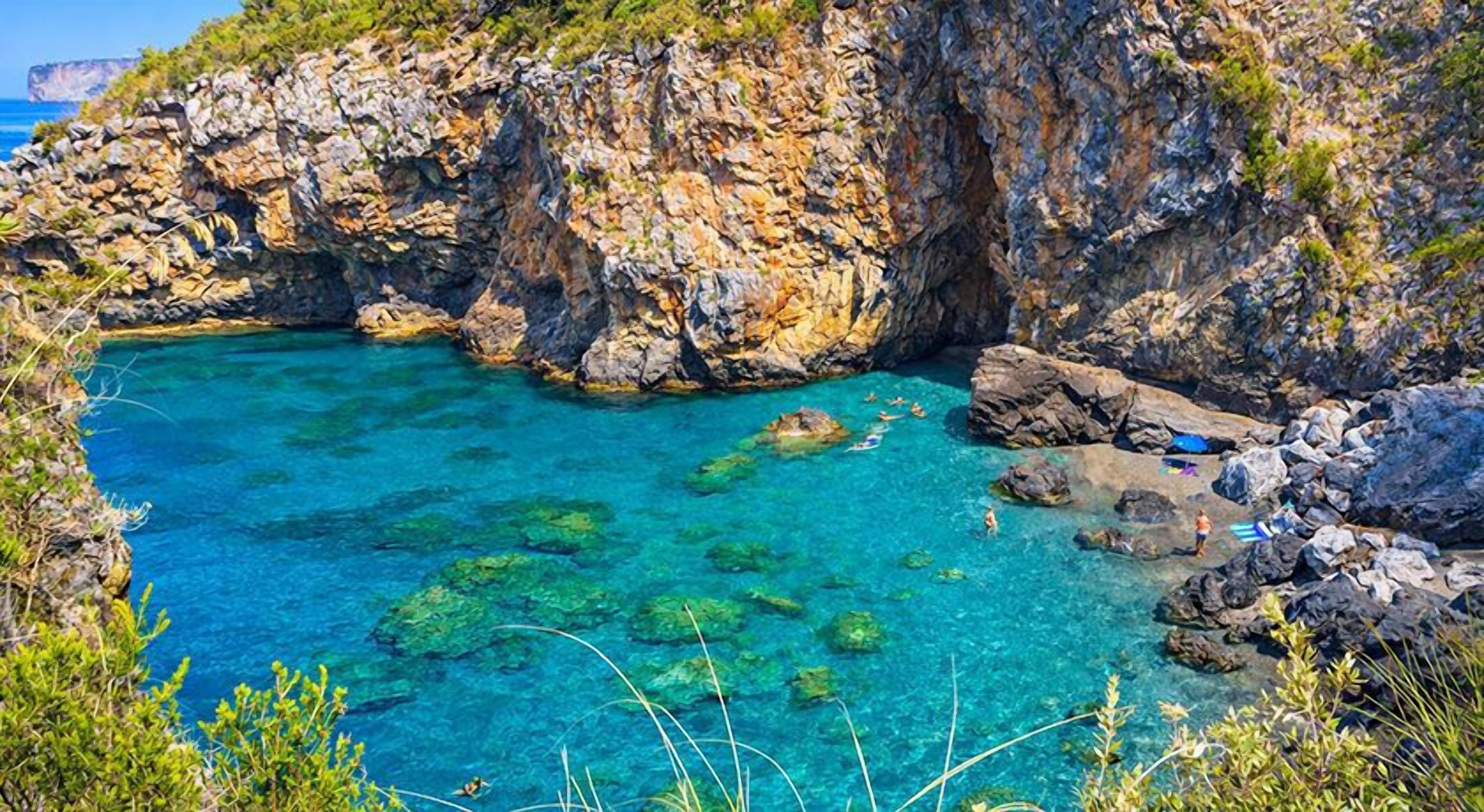 A rocky coastal landscape with clear blue water, some vegetation, and a cliff.