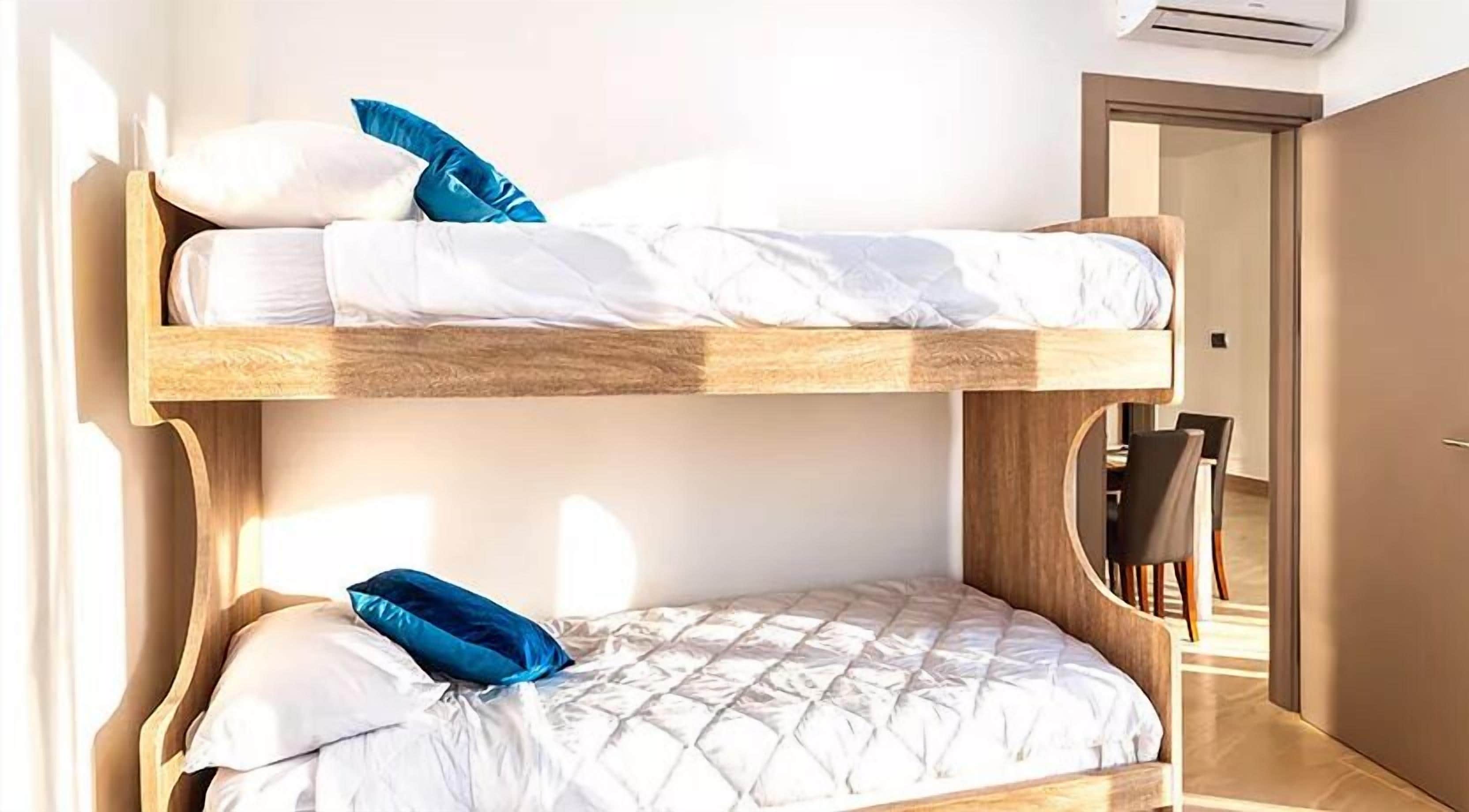 Une chambre avec un lit superposé, une structure en bois, une literie blanche et un oreiller bleu.
