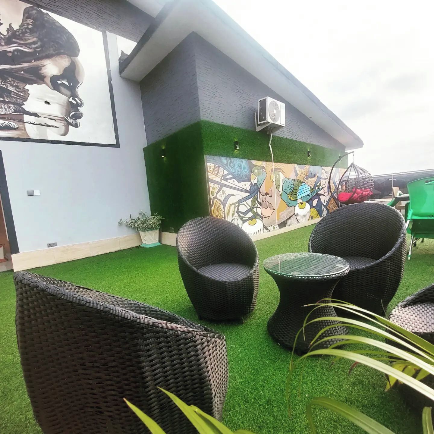 An outdoor seating area with wicker furniture, a mural on the wall, and artificial grass.