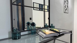 Een moderne badkamer met een glazen wastafel, een grote spiegel en decoratieve items, waaronder een vetplant en een lijstwerk met kunstwerk.