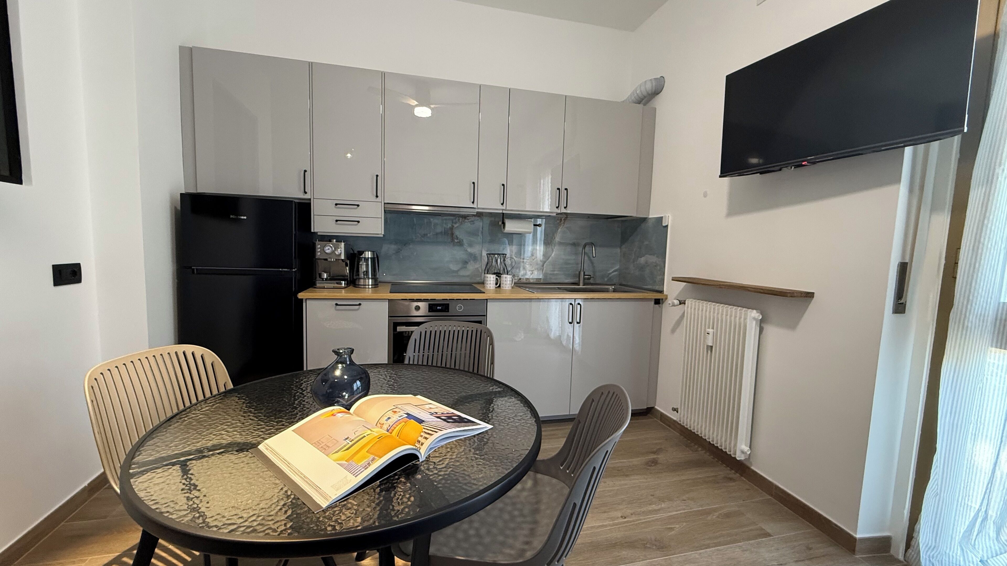Cocina compacta con electrodomésticos modernos, una mesa de comedor con sillas y un televisor de pantalla plana en la pared.